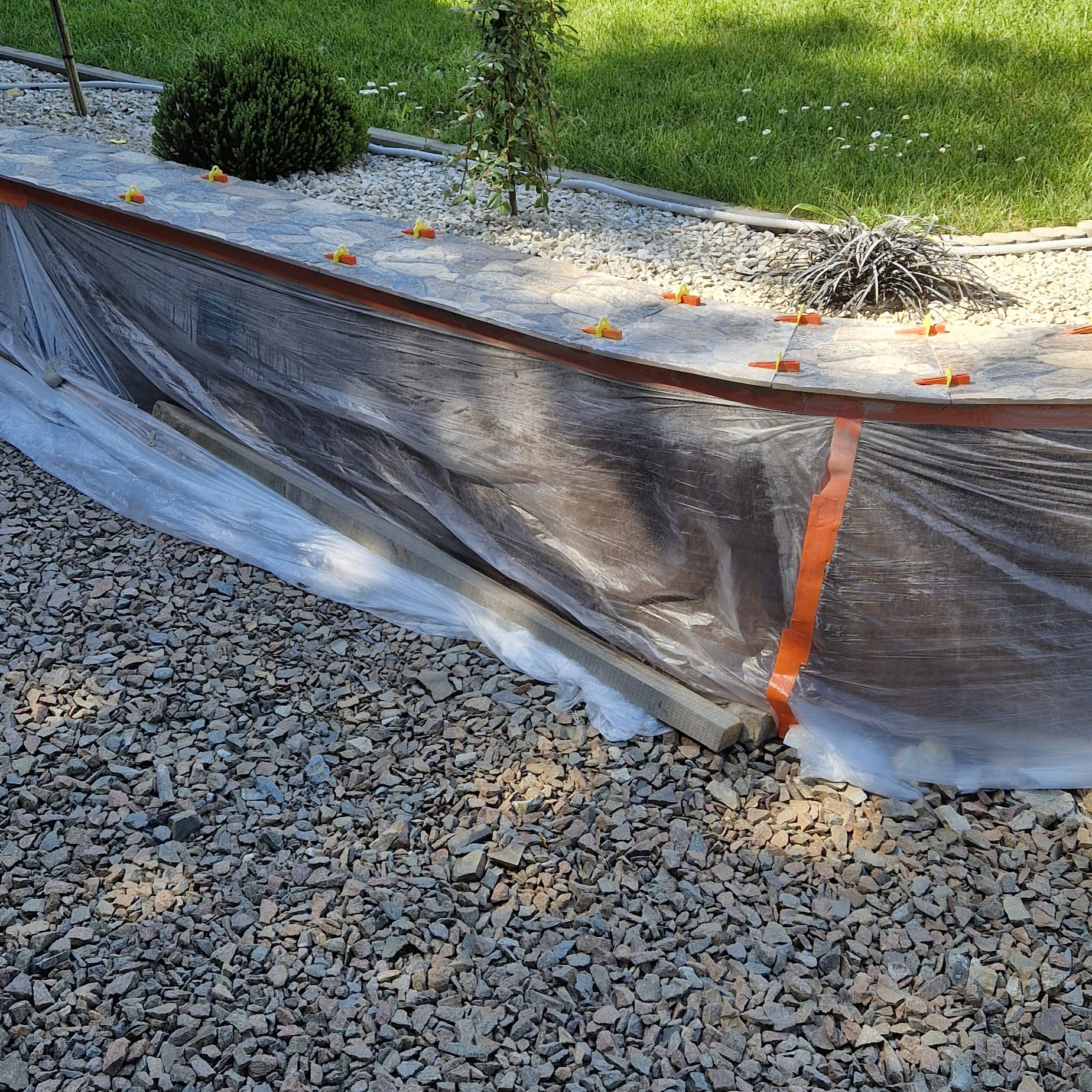 Układanie płytek na zewnątrz: widoczne poziomice i plastikowa folia ochronna na tle żwirowego podłoża.