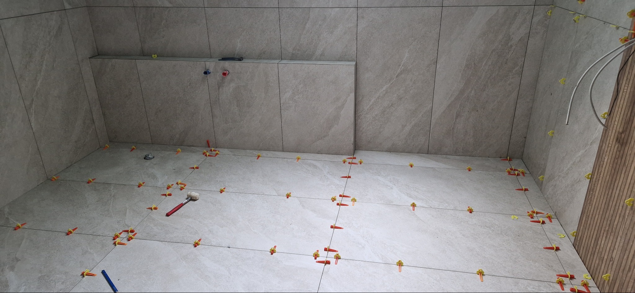 Ułożone płytki podłogowe i ścienne w łazience, z wykorzystaniem systemu poziomowania płytek (klipsy i kliny) oraz gumowego młotka.