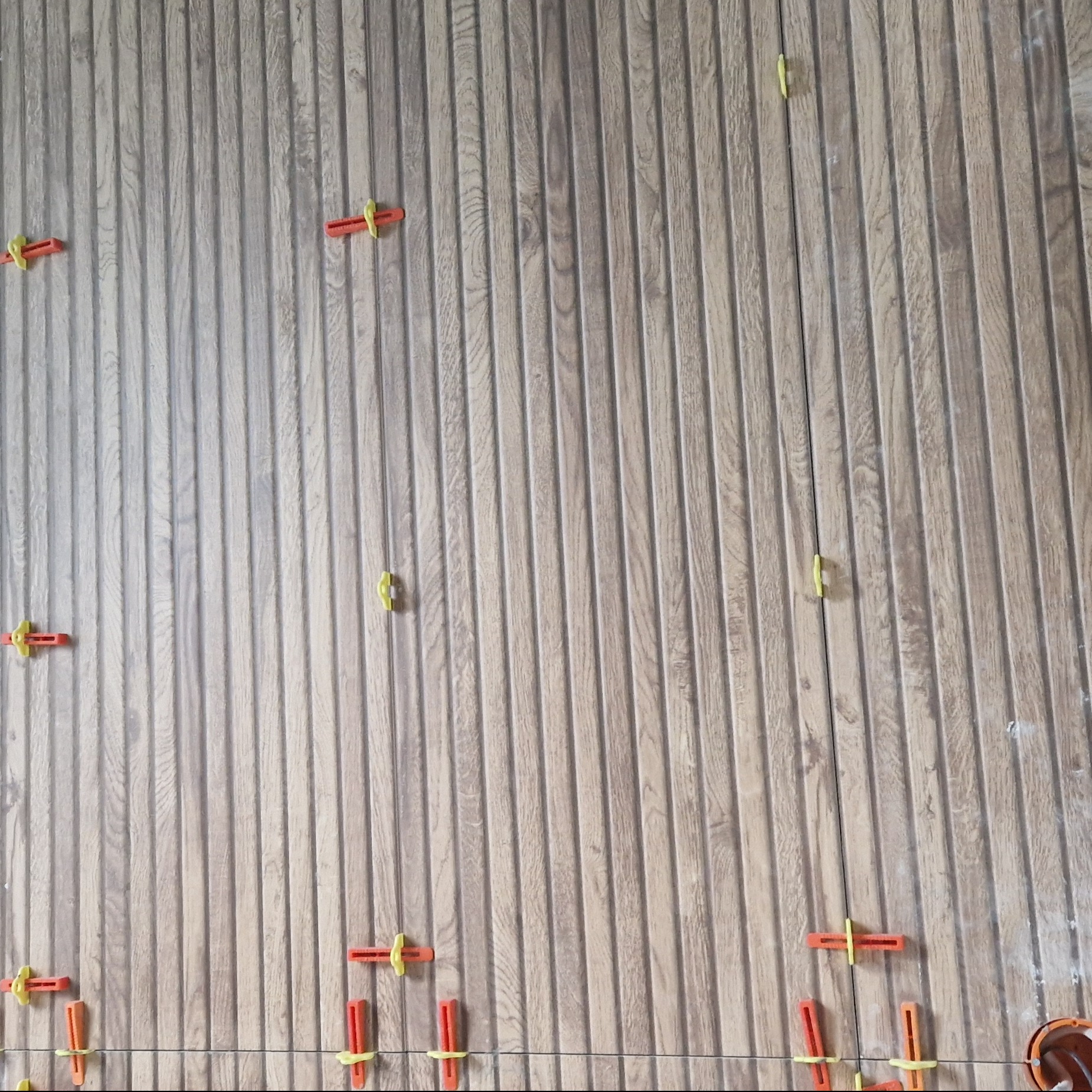 Układanie płytek imitujących drewno na ścianie z użyciem systemu poziomowania płytek w Sułkowicach, widoczne klipsy i kliny.