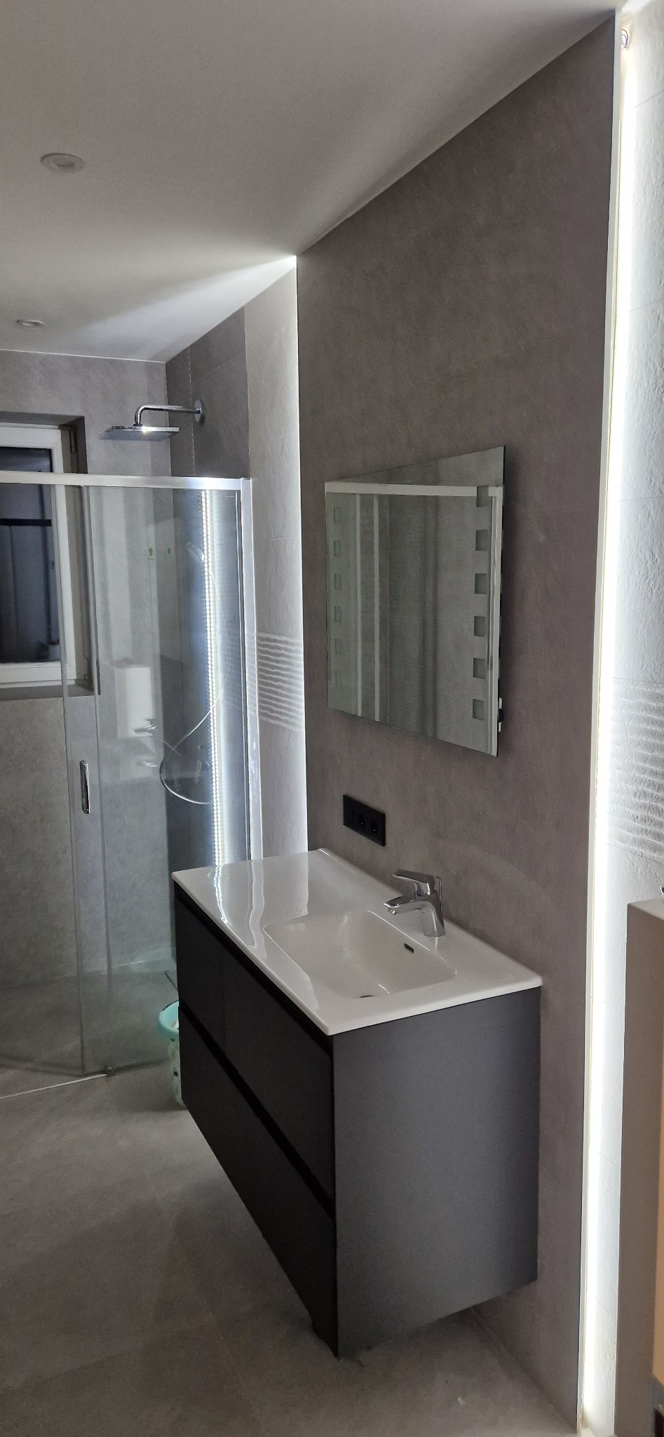 Nowoczesna łazienka z szarą armaturą, kabiną prysznicową typu walk-in i podświetlanym lustrem z dekoracyjnymi kwadratami