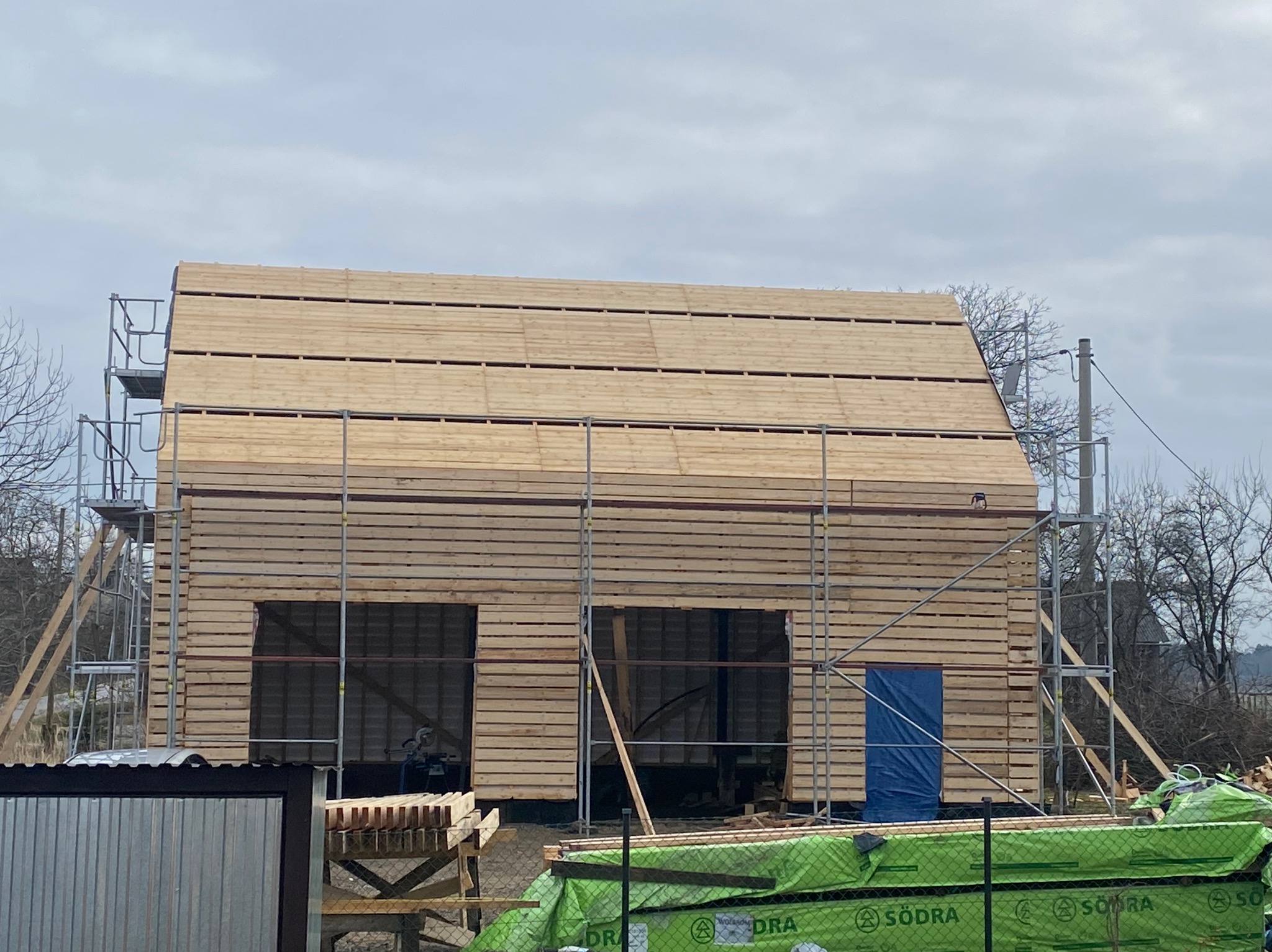 Konstrukcja domu w trakcie budowy, widoczne drewniane bale i rusztowania, z boku leżą materiały budowlane.