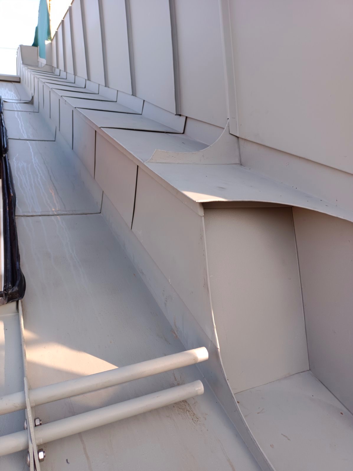 Szare, metalowe orynnowanie dachu z widocznymi elementami mocującymi i śladami zacieków.