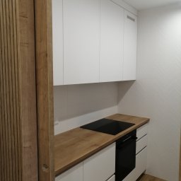 Meble Andrii Pavlenko - Nowoczesna kuchnia: białe szafki z drewnianym blatem, płyta indukcyjna i piekarnik, drewniane panele dekoracyjne na ścianie.