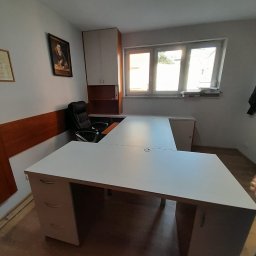 Meble Andrii Pavlenko - Białe, narożne biurko z szufladami i szafką wiszącą w jasnym biurze, widok z przodu