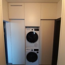 Meble Andrii Pavlenko - Biała zabudowa meblowa z pralką i suszarką w kolumnie, widok z perspektywy korytarza, minimalistyczny design.