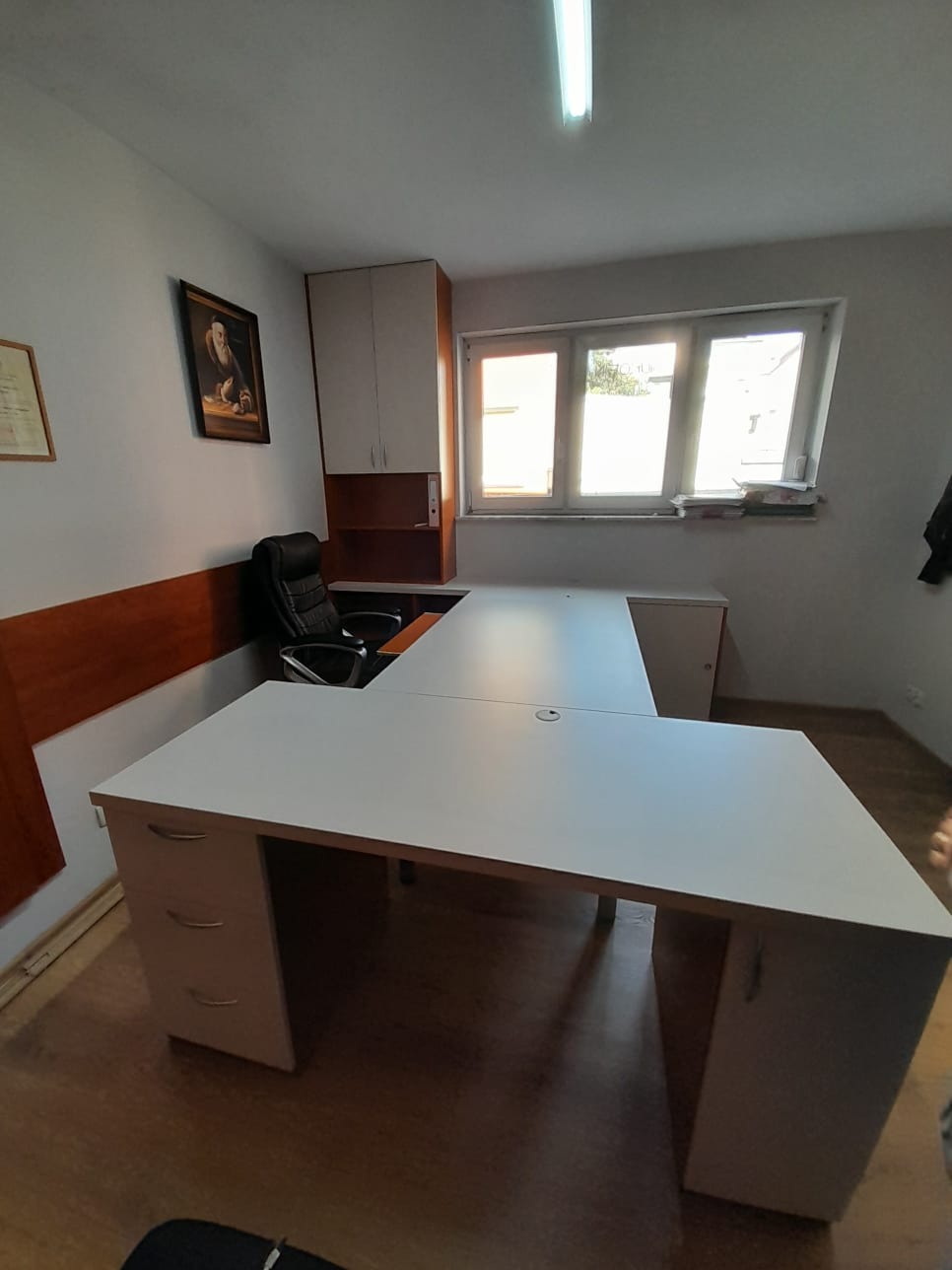 Białe, narożne biurko z szufladami i szafką wiszącą w jasnym biurze, widok z przodu