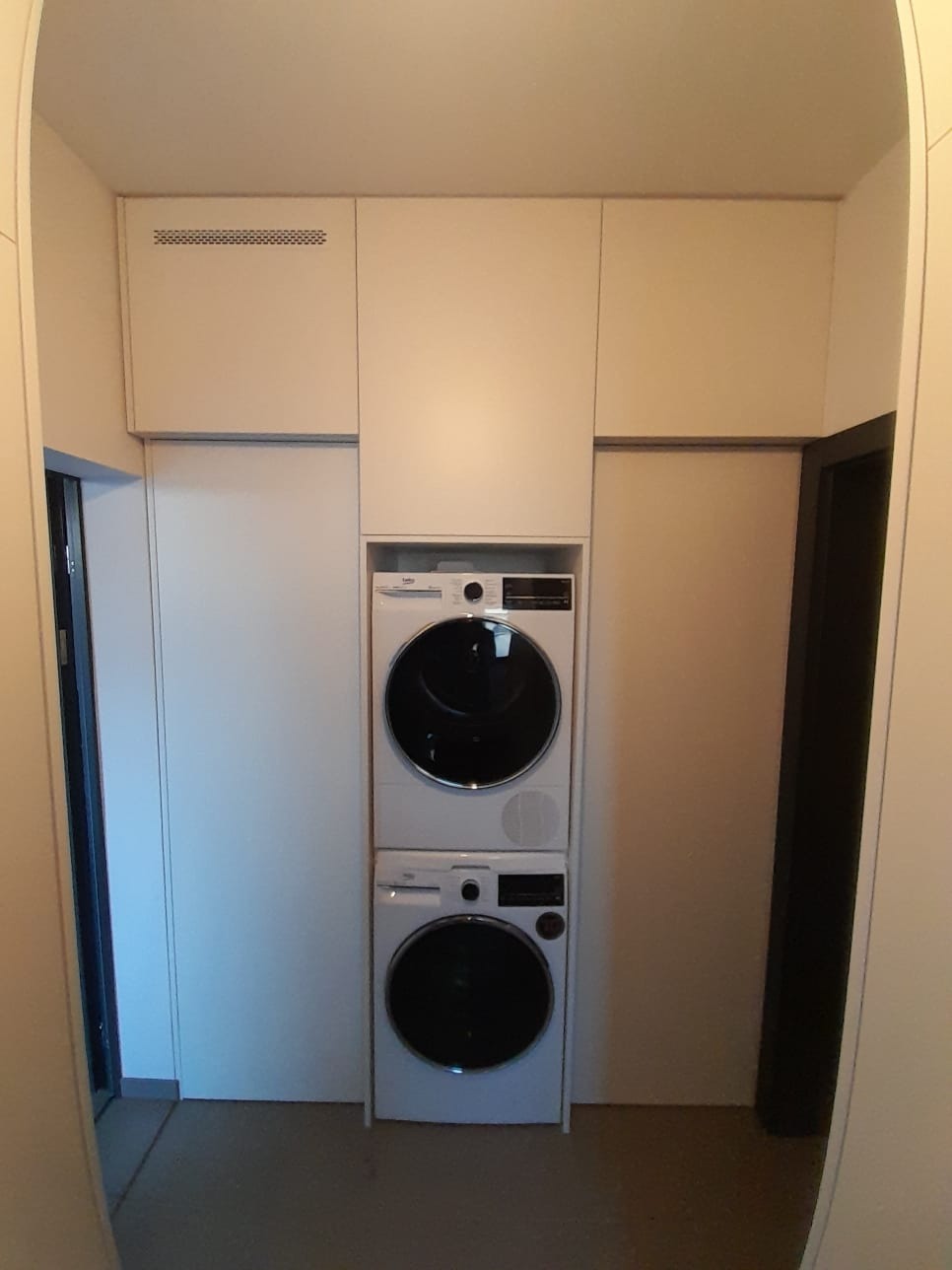 Biała zabudowa meblowa z pralką i suszarką w kolumnie, widok z perspektywy korytarza, minimalistyczny design.