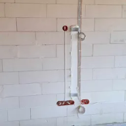 Instalacja elektryczna w trakcie montażu w nowym budynku: przewody prowadzone w bruzdach w ścianie z betonu komórkowego, puszki podtynkowe zamontowane, przewody zabezpieczone pianką montażową.
