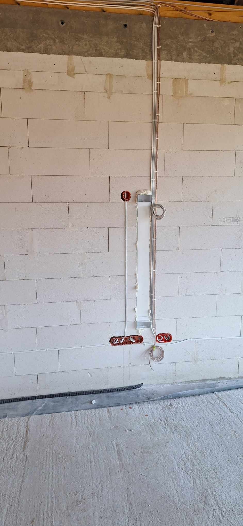 Instalacja elektryczna w trakcie montażu w nowym budynku: przewody prowadzone w bruzdach w ścianie z betonu komórkowego, puszki podtynkowe zamontowane, przewody zabezpieczone pianką montażową.