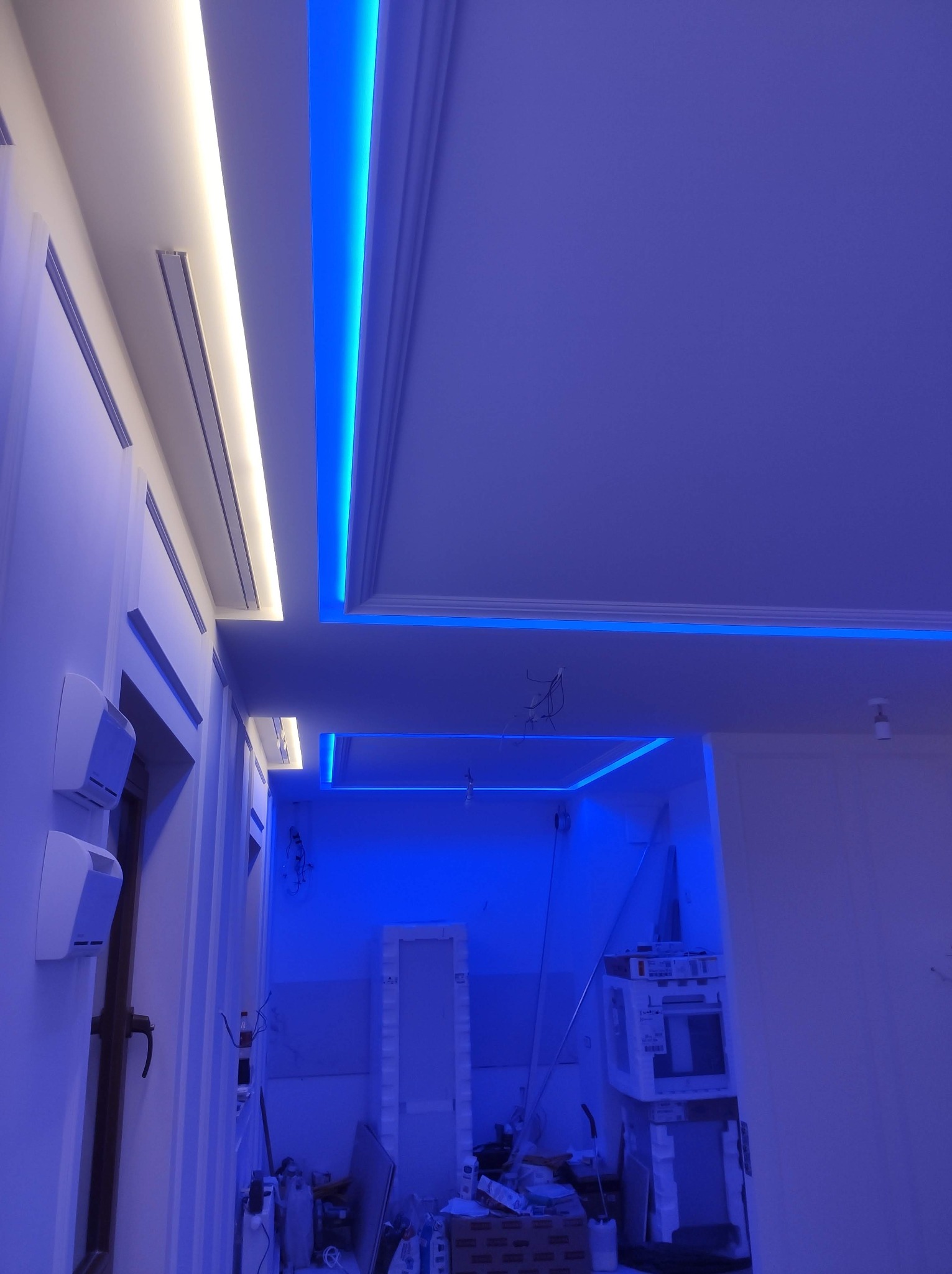 Podwieszany sufit z dekoracyjnym oświetleniem LED w kolorze białym i niebieskim. Widoczne elementy wykończeniowe i przewody elektryczne.