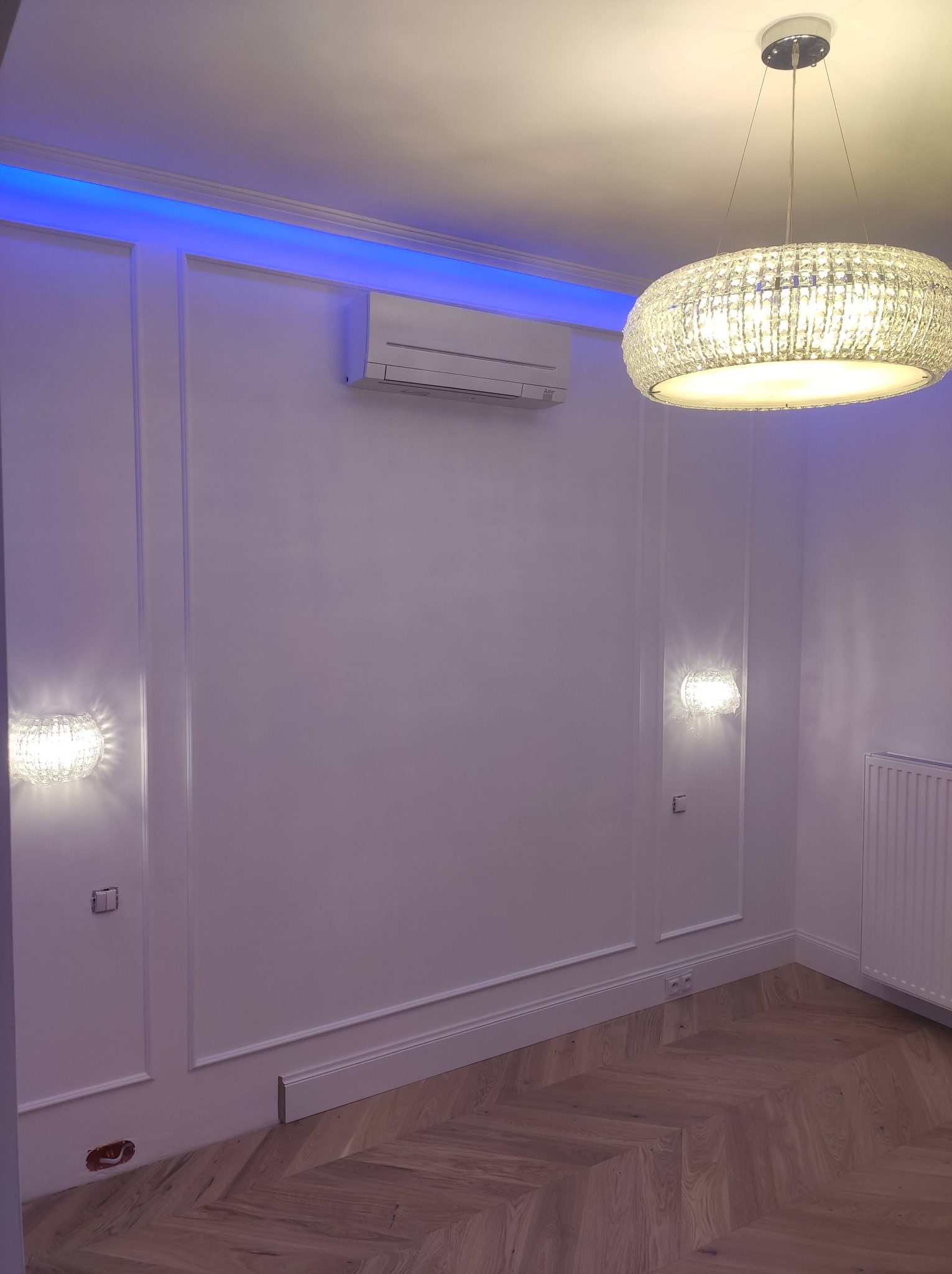 Eleganckie wnętrze z białymi ścianami zdobionymi sztukaterią, parkietem w jodełkę, klimatyzacją, oświetleniem LED i kryształowym żyrandolem.