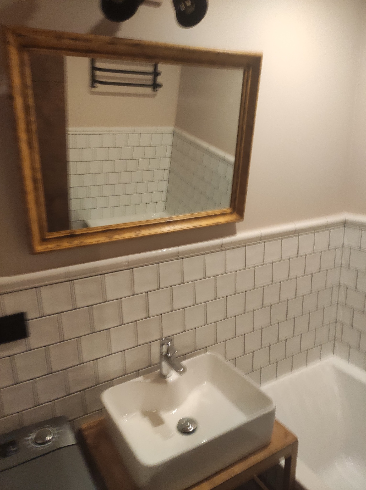 Nowoczesna łazienka z umywalką nablatową, białe płytki typu metro na ścianach i złote lustro odbijające fragment kabiny prysznicowej. Minimalistyczny design.