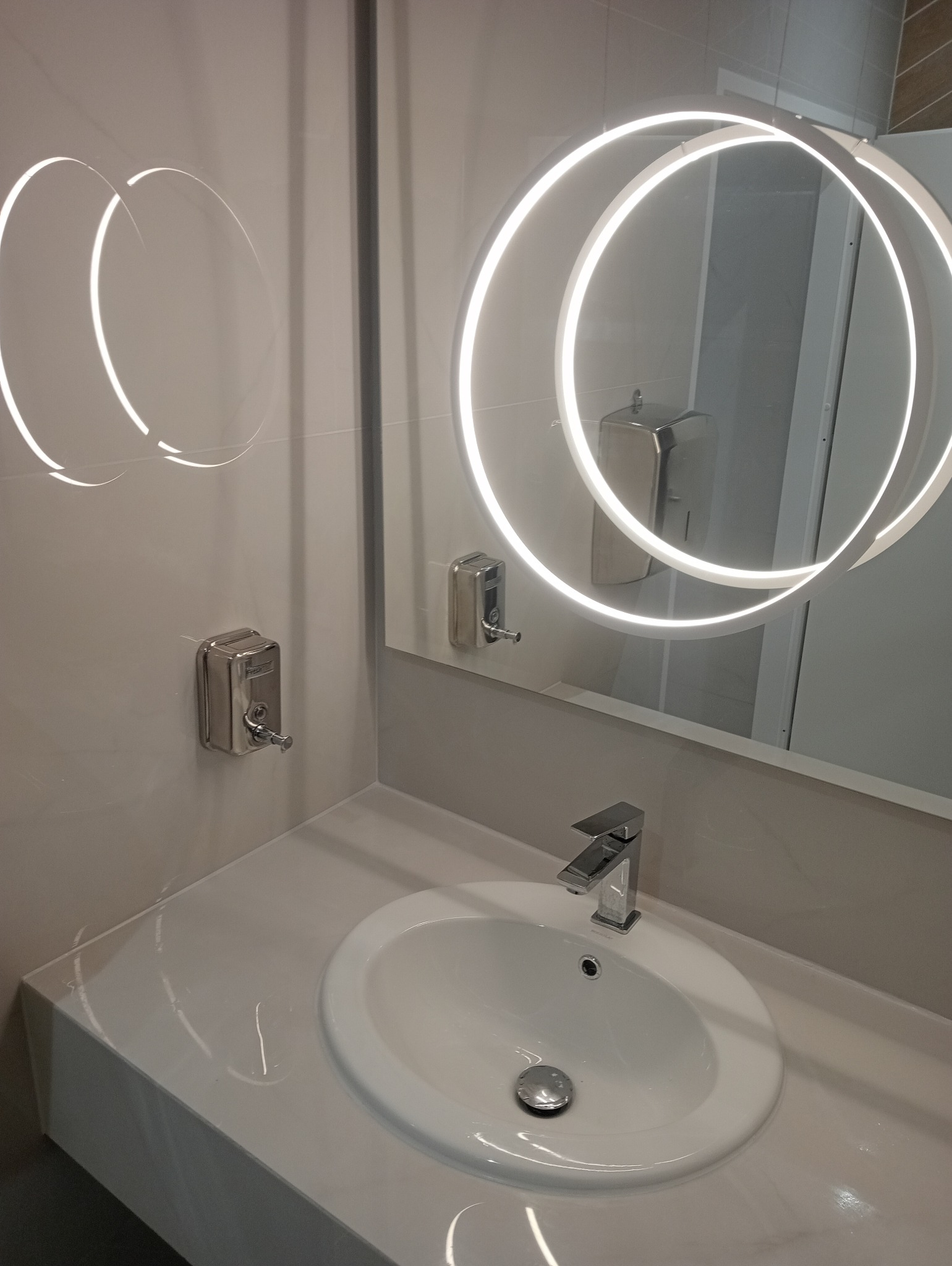 Nowoczesna umywalka z podświetlanym lustrem w łazience po remoncie w Warszawie. Minimalistyczny design, chromowana bateria i dozownik mydła.