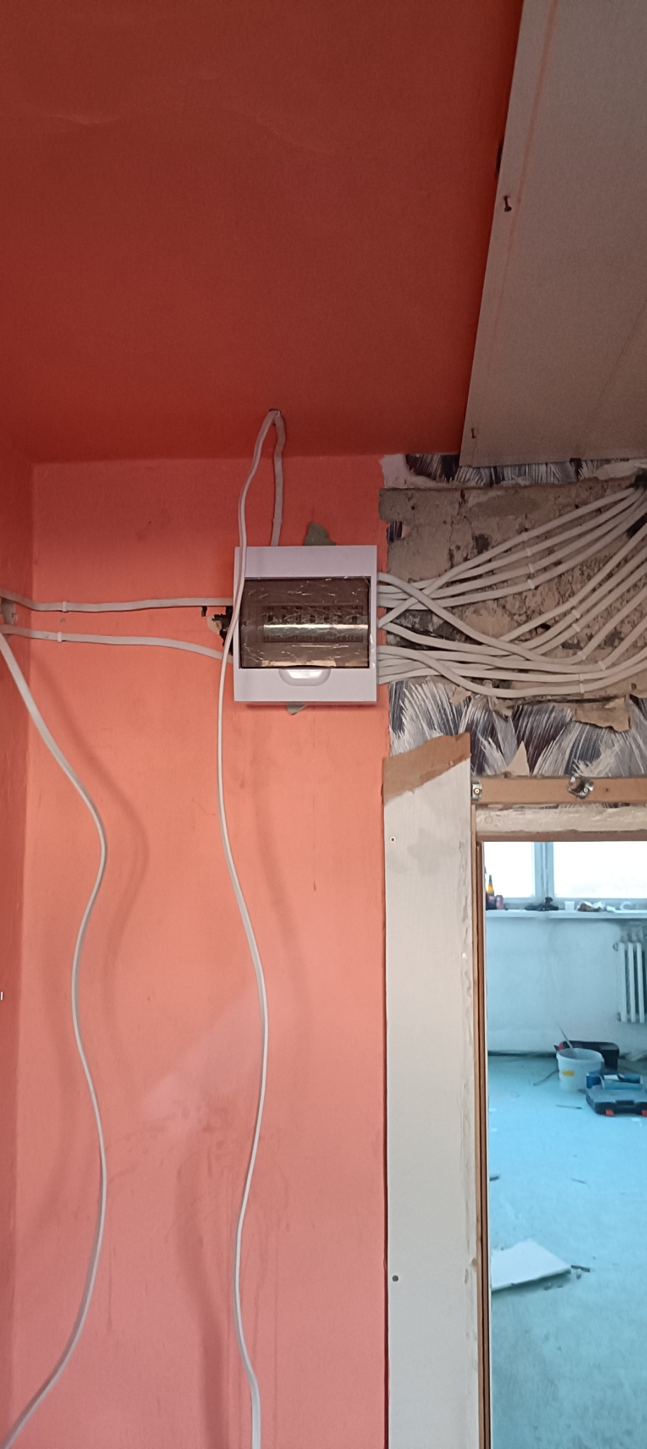 Nowa skrzynka elektryczna zamontowana na ścianie w trakcie remontu, widoczne kable w ścianie i świeżo pomalowana ściana na różowo.