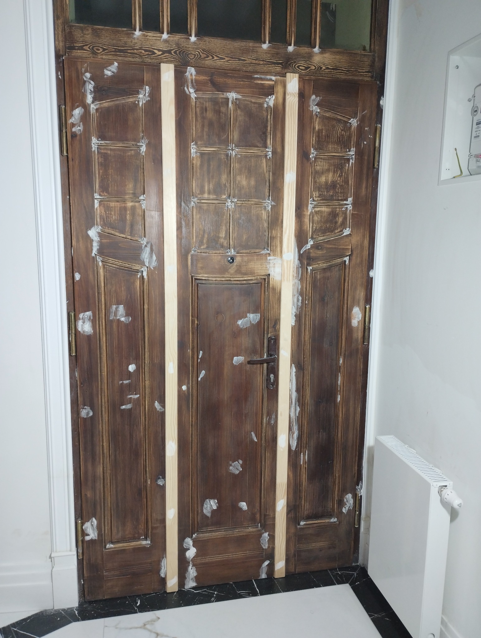 Renowacja drewnianych drzwi wewnętrznych: szpachlowanie ubytków w drewnie, widoczne listwy maskujące, przygotowanie do malowania.