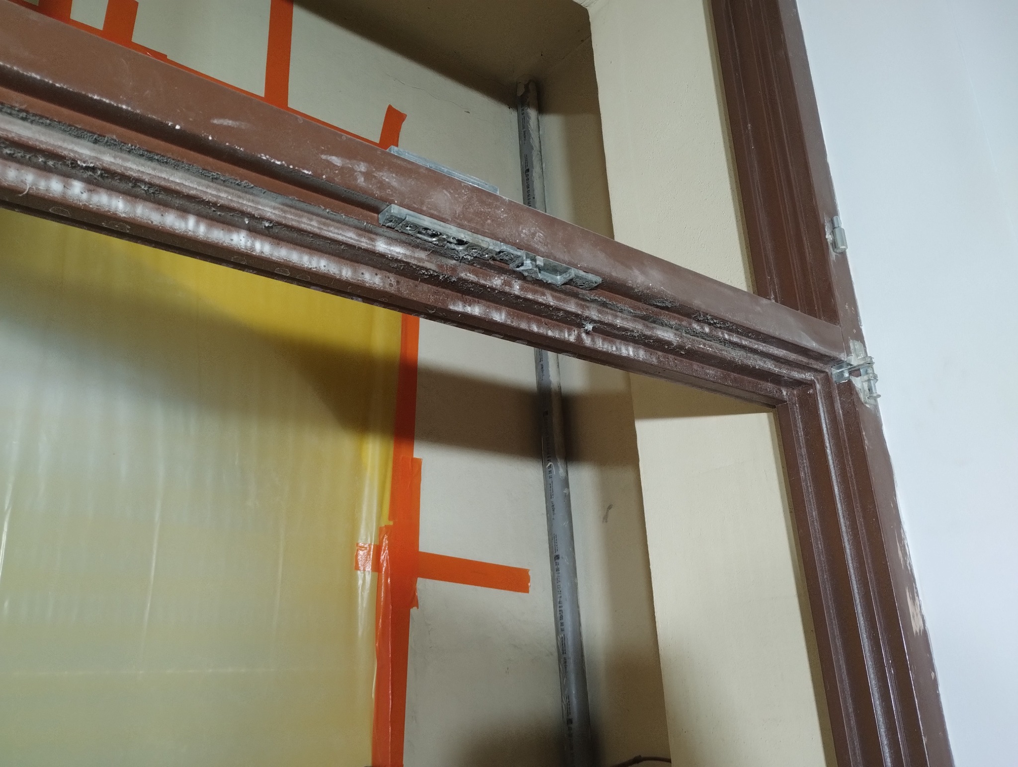 Przygotowanie do malowania ościeżnicy drzwiowej, zabezpieczona folią i taśmą, widoczne ślady szpachli i montaż zawiasów.