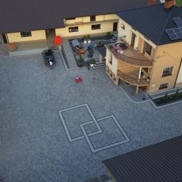 PG BRUK - Rozległy dziedziniec z kostki brukowej w geometryczny wzór, otoczony budynkami z panelami słonecznymi, widok z lotu ptaka.