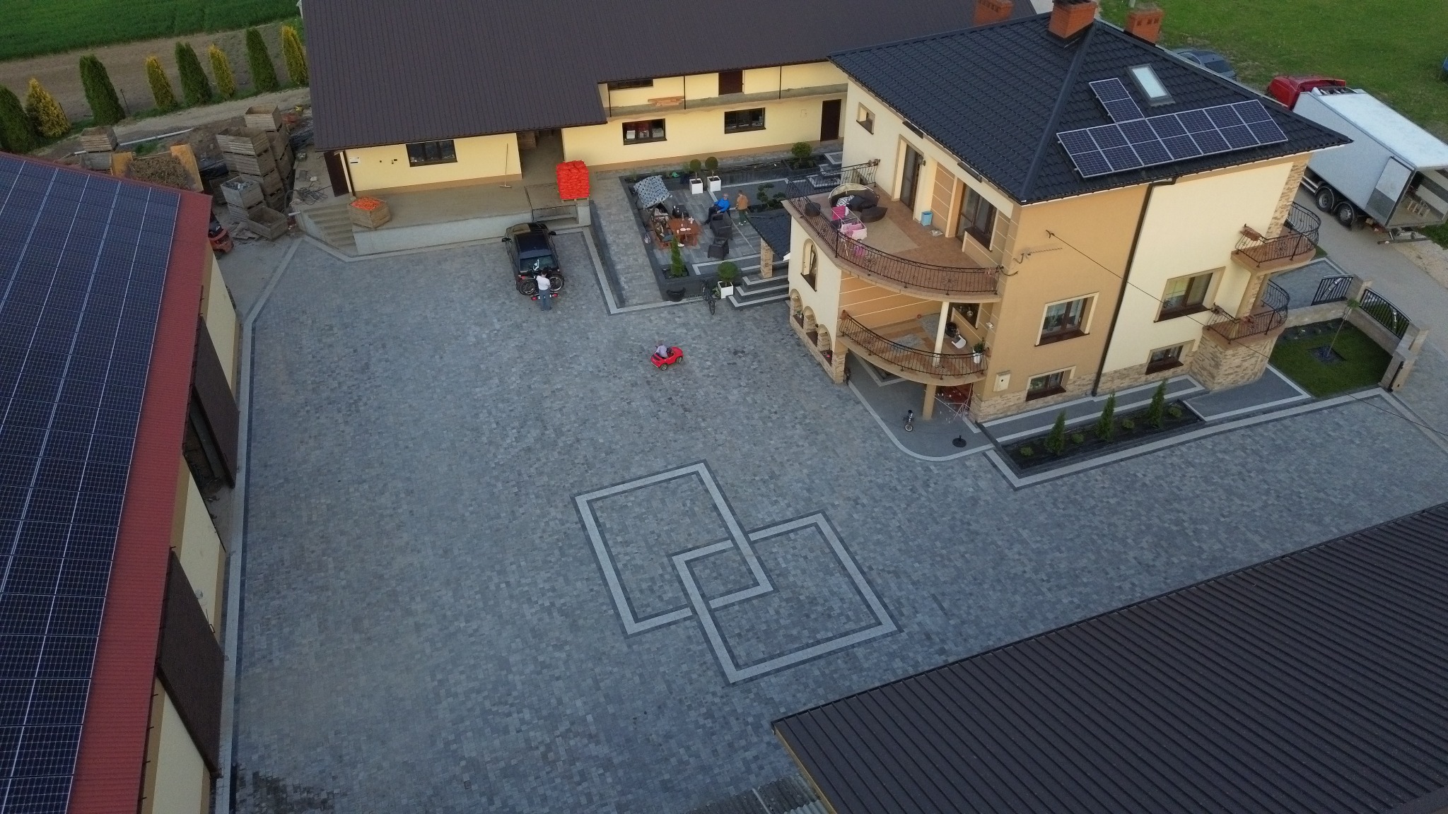 Rozległy dziedziniec z kostki brukowej w geometryczny wzór, otoczony budynkami z panelami słonecznymi, widok z lotu ptaka.