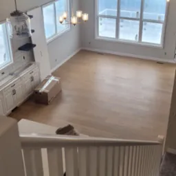 Widok z góry na jasne, świeżo wykończone wnętrze domu w Świnnej, z drewnianą podłogą, białymi ścianami i schodami z białą balustradą. Widoczne okna z folią ochronną, lampy wiszące i karton...