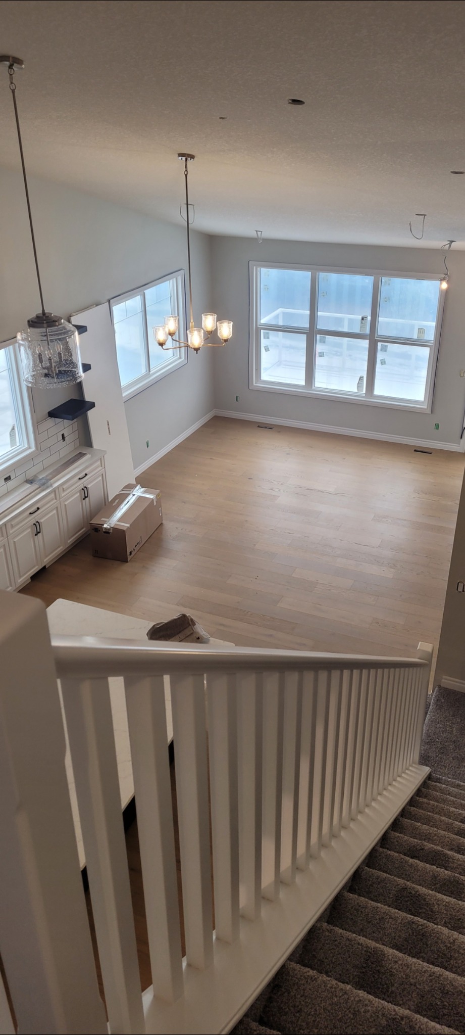 Widok z góry na jasne, świeżo wykończone wnętrze domu w Świnnej, z drewnianą podłogą, białymi ścianami i schodami z białą balustradą. Widoczne okna z folią ochronną, lampy wiszące i karton...