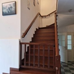 Mateusz Górski - Klasyczne, ciemne stopnie z drewna prowadzące na górę, z drewnianą balustradą i poręczą, na ścianie wiszą obrazy, widoczna podłoga w szachownicę i drzwi.