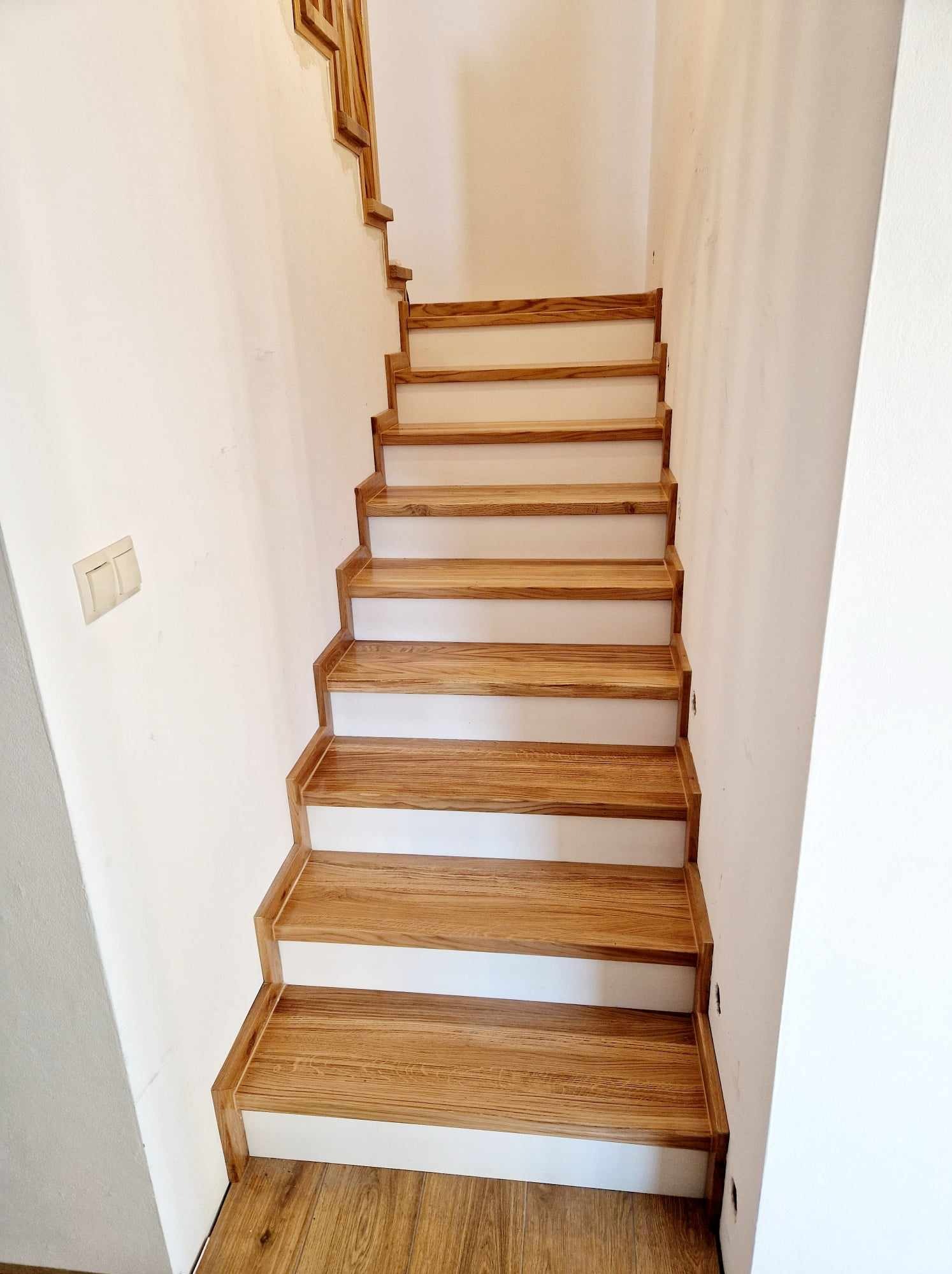 Dębowe schody z litego drewna, zamontowane na betonowej konstrukcji, widoczne z dołu, z białymi podstopnicami i drewnianą listwą przyścienną.