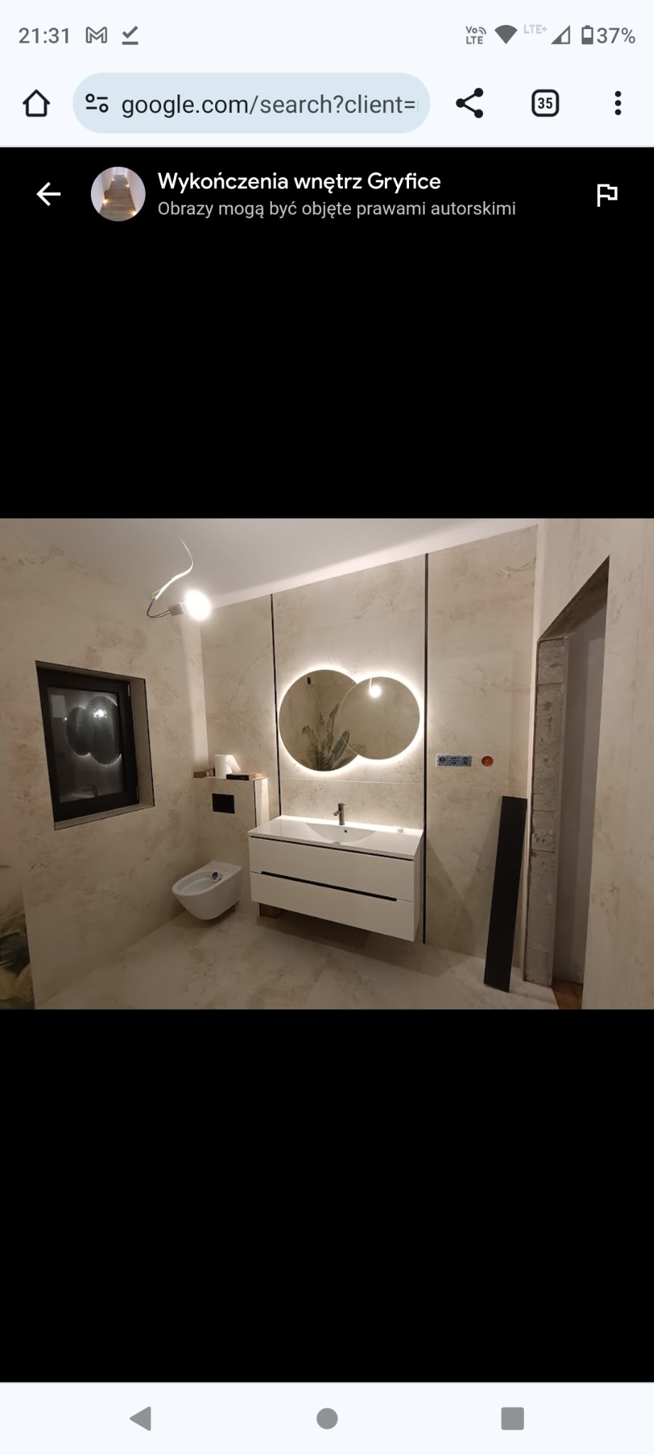 Nowoczesna łazienka z beżowymi ścianami, białym wiszącym bidetem i szafką pod umywalkę z dwiema szufladami, nad którą wiszą dwa okrągłe lustra z podświetleniem LED.