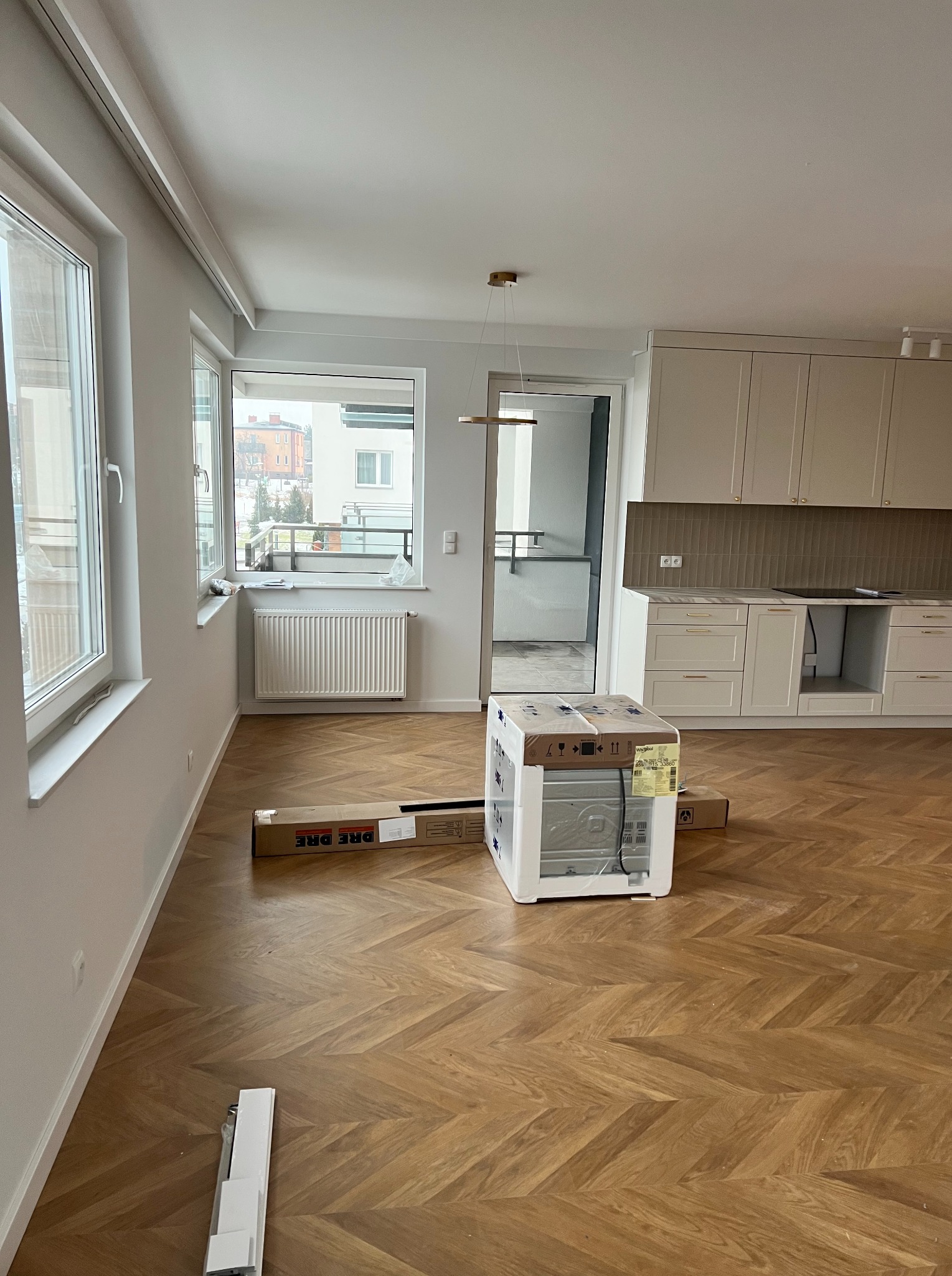 Nowe mieszkanie z parkietem w jodełkę, zamontowaną kuchnią i rozpakowaną zmywarką w kartonie, czeka na dalsze prace wykończeniowe.
