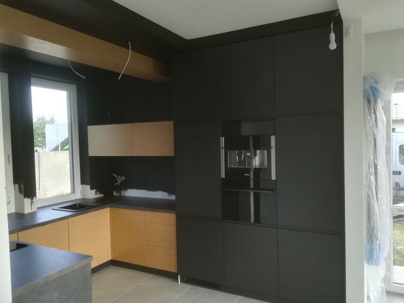 Nowoczesna kuchnia z zabudową w odcieniach czerni i jasnego drewna, z wbudowanym ekspresem do kawy i elementami wykończeniowymi w trakcie prac.