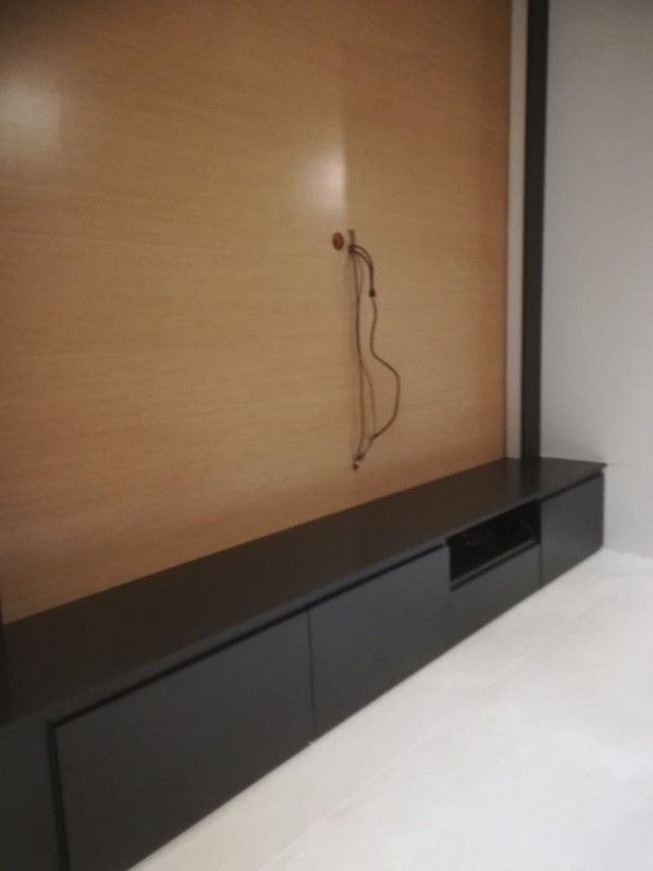 Część zabudowy meblowej z drewnianym panelem ściennym, czarnymi szafkami dolnymi z gładkimi frontami i wystającymi kablami ze ściany.