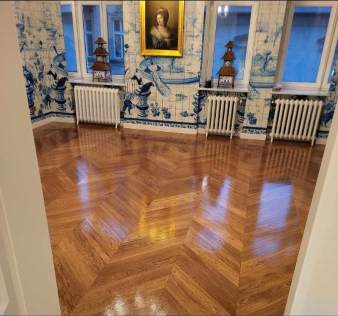 Parkiet ułożony we wzór jodełki w przestronnym pokoju w Warszawie, z widocznymi grzejnikami i dekoracyjnymi płytkami na ścianach.