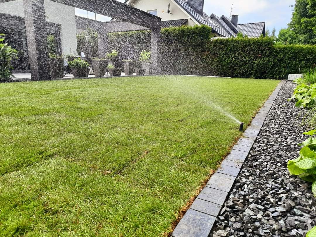 Automatyczne nawadnianie trawnika z rolki, widok na zraszacze, obrzeża z kostki i rabatę z grysu.