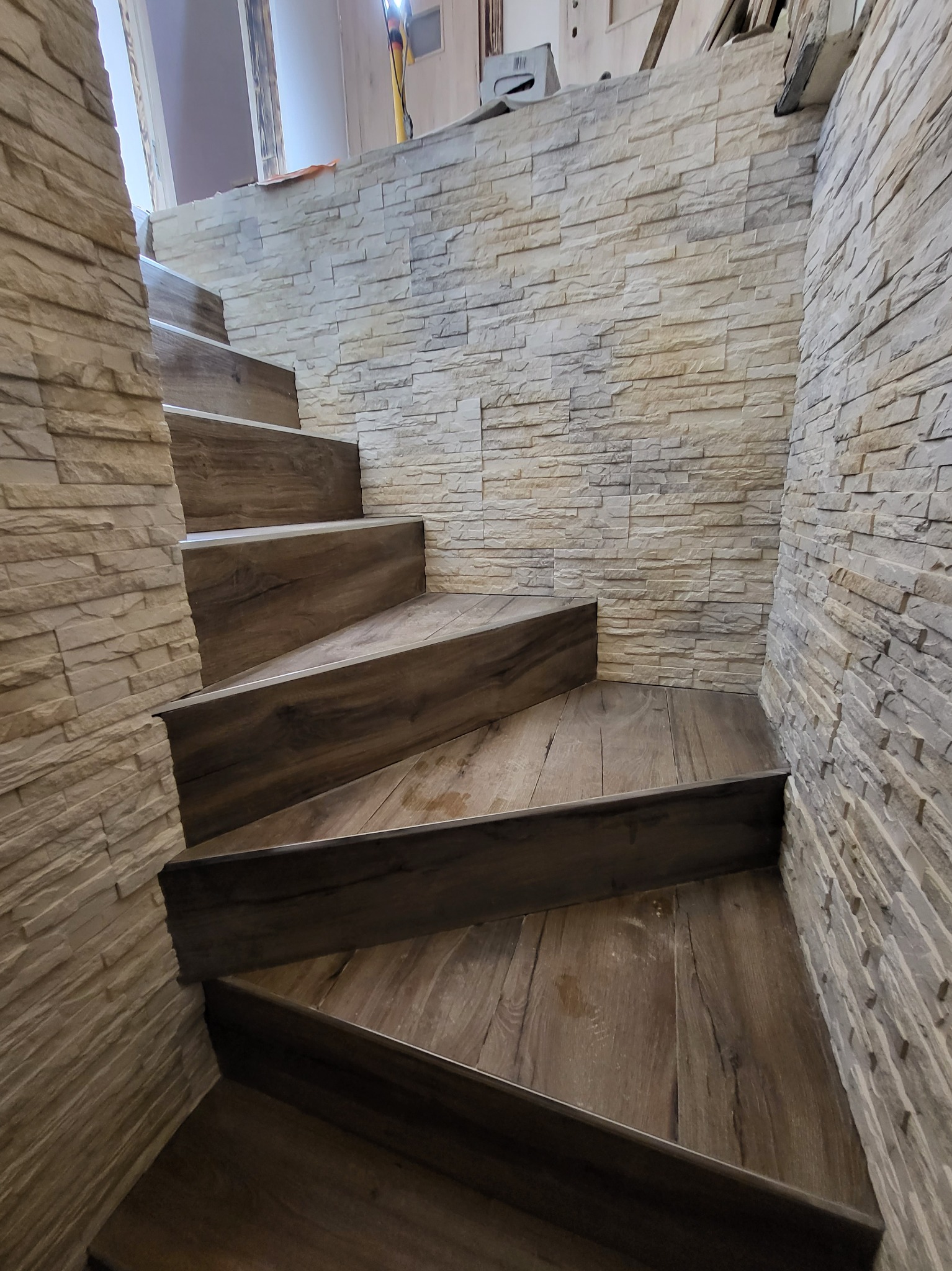 Schody z drewnopodobnymi stopniami i kamienną okładziną ściany w odcieniach beżu i brązu, widok z dołu.