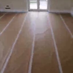 złota rączka - Przygotowany do malowania parkiet z taśmą maskującą przy listwach podłogowych i wokół drzwi balkonowych, ściany w jasnym kolorze.