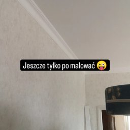 złota rączka - Ściana z fakturą i listwą dekoracyjną pod sufitem, przygotowana do malowania. Widoczny fragment futryny drzwi i element wyposażenia wnętrza w tle.