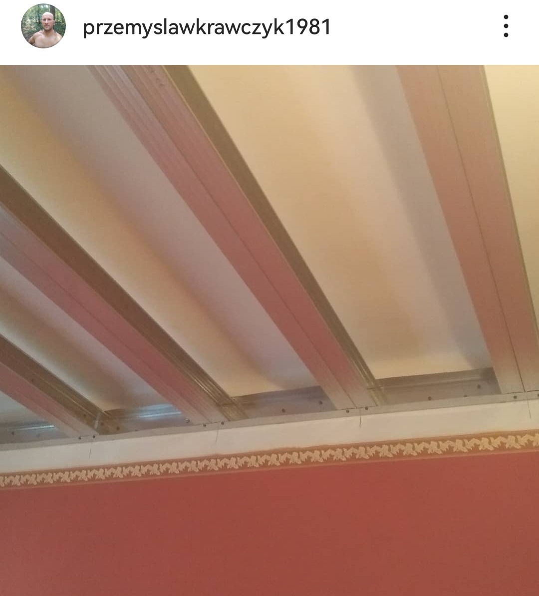 Montaż metalowej konstrukcji sufitu podwieszanego z widocznymi profilami na tle fragmentu ściany z bordiurą.