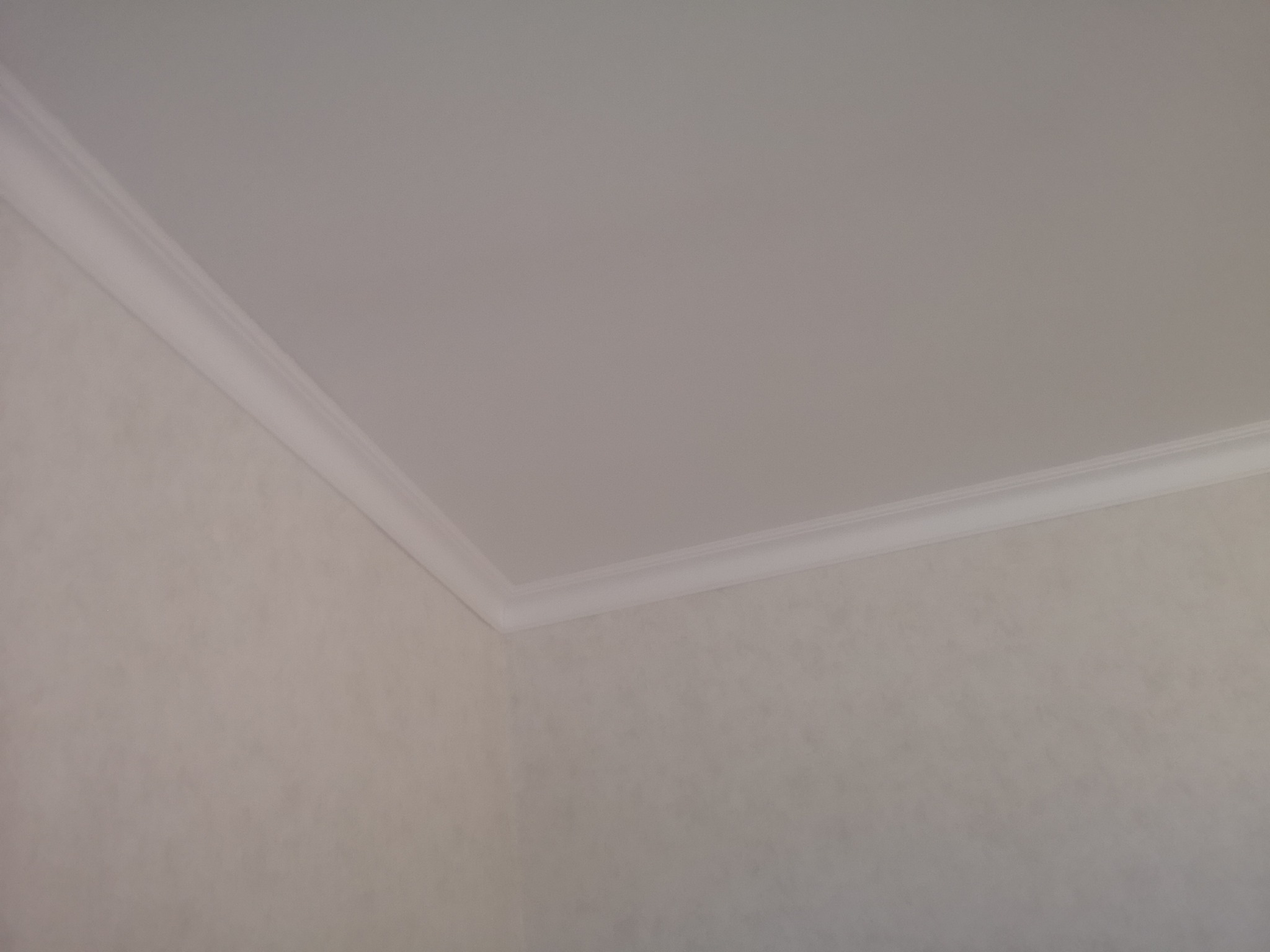 Jasny pokój z wykończonym sufitem i ścianami, widoczne połączenie sufitu ze ścianą wykończone ozdobnym, białym profilem.