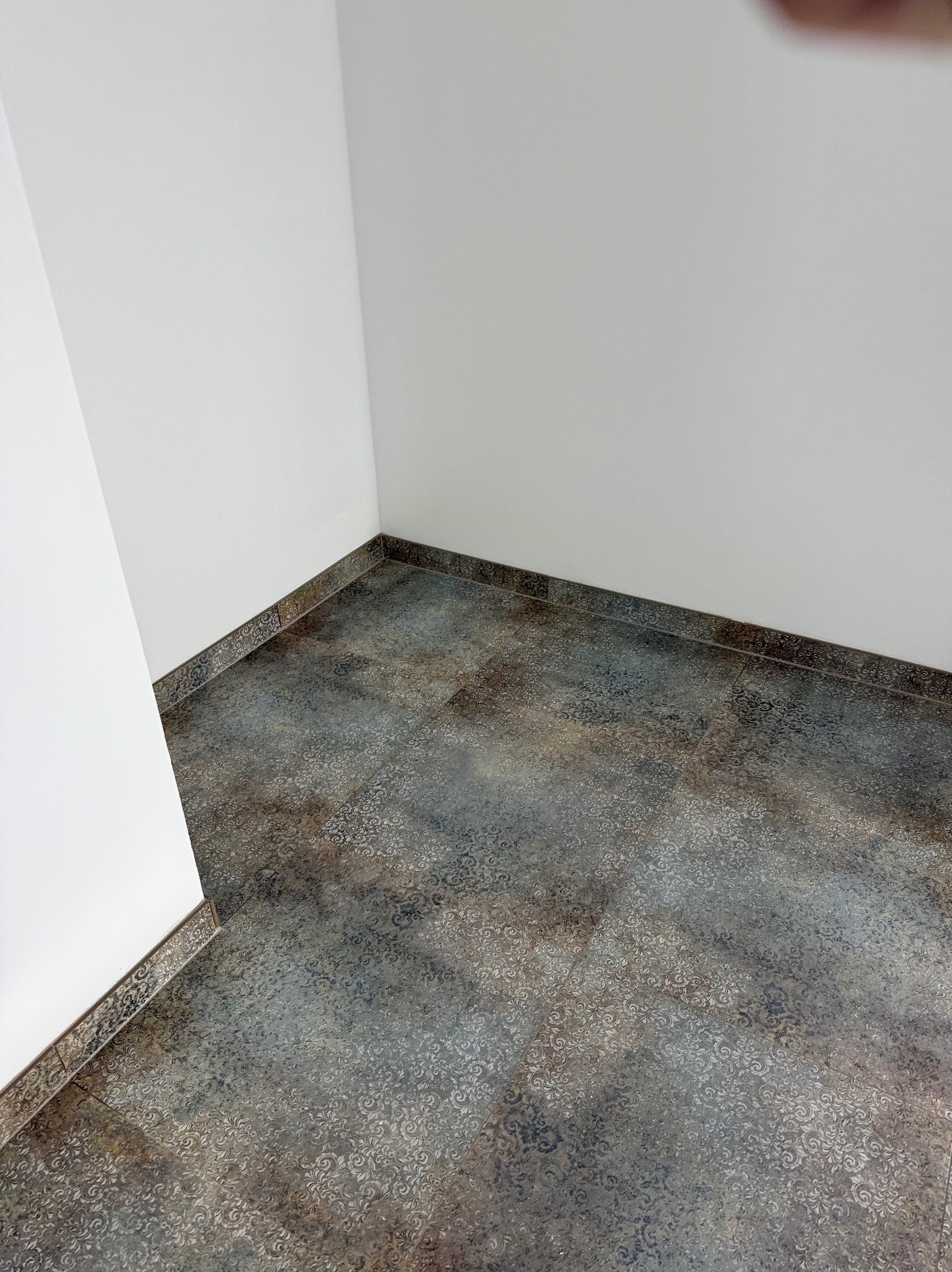 Ukończone układanie płytek podłogowych z dekoracyjnym wzorem w rogu pomieszczenia w Bydgoszczy. Widoczne białe ściany i ciemne fugi.