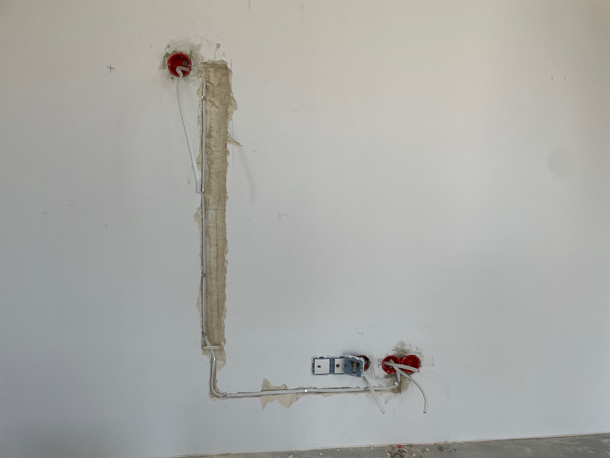 Świeżo położone przewody elektryczne w bruzdach i puszkach w białej ścianie, przygotowane do dalszych prac wykończeniowych.