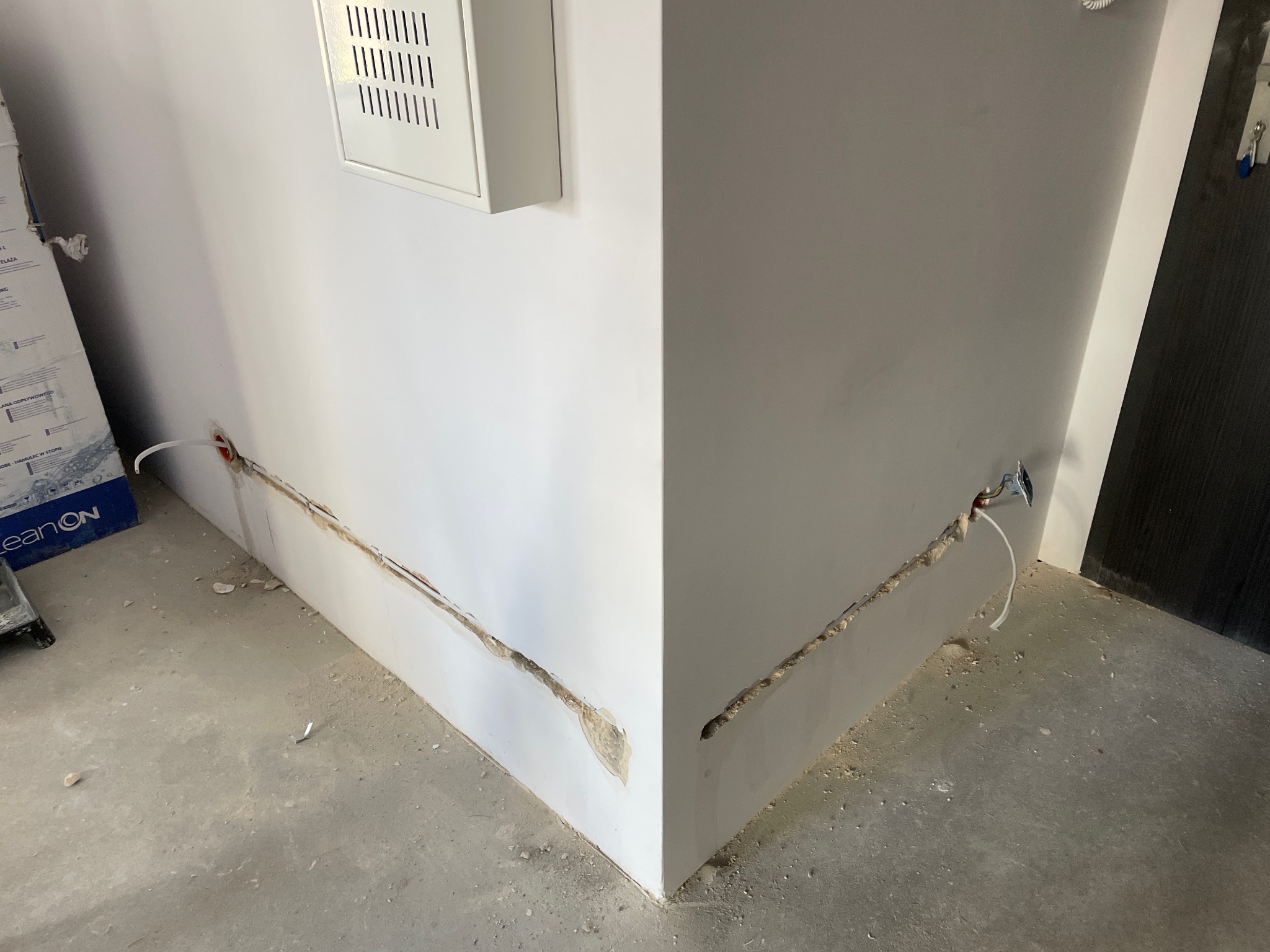 Wykute bruzdy w ścianie pod kable elektryczne, widoczna puszka instalacyjna, skrzynka rozdzielcza na ścianie, przygotowanie do montażu instalacji elektrycznej.