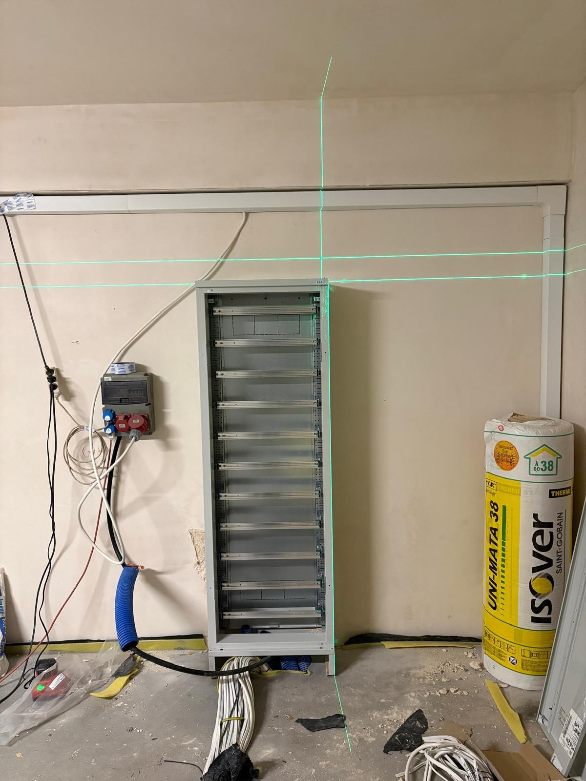 Rozdzielnica elektryczna w trakcie montażu w Katowicach, widoczne kable, peszle i poziomica laserowa. Prace instalacyjne w surowym stanie.