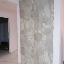 Studio mebli FABIANI - Dwudrzwiowa szafa wnękowa z subtelnym, roślinnym wzorem na jasnoszarym tle, wkomponowana w białe wnętrze z marmurową podłogą i widocznym fragmentem korytarza.