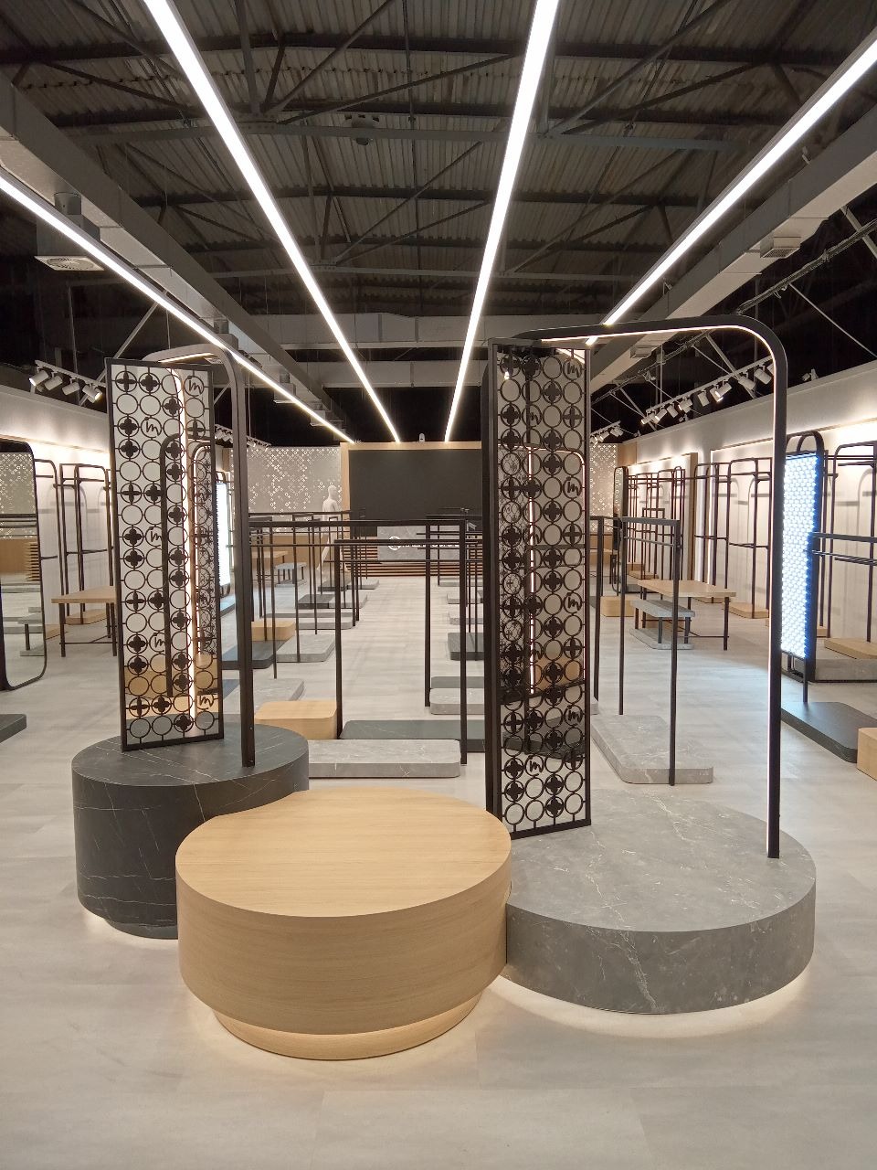 Nowoczesna aranżacja wnętrza sklepu odzieżowego z okrągłymi podestami z drewna i marmuru, metalowymi wieszakami i oświetleniem LED. Minimalistyczny design.