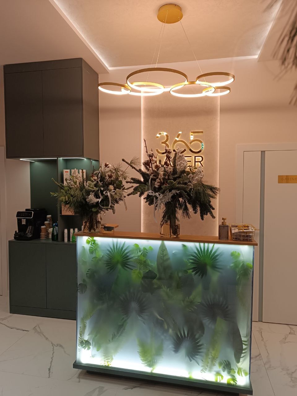 Recepcja z szafką w salonie. Podświetlany blat z motywem roślinnym, dekoracje kwiatowe, nowoczesna lampa. Eleganckie wykończenie, marmurowa podłoga.