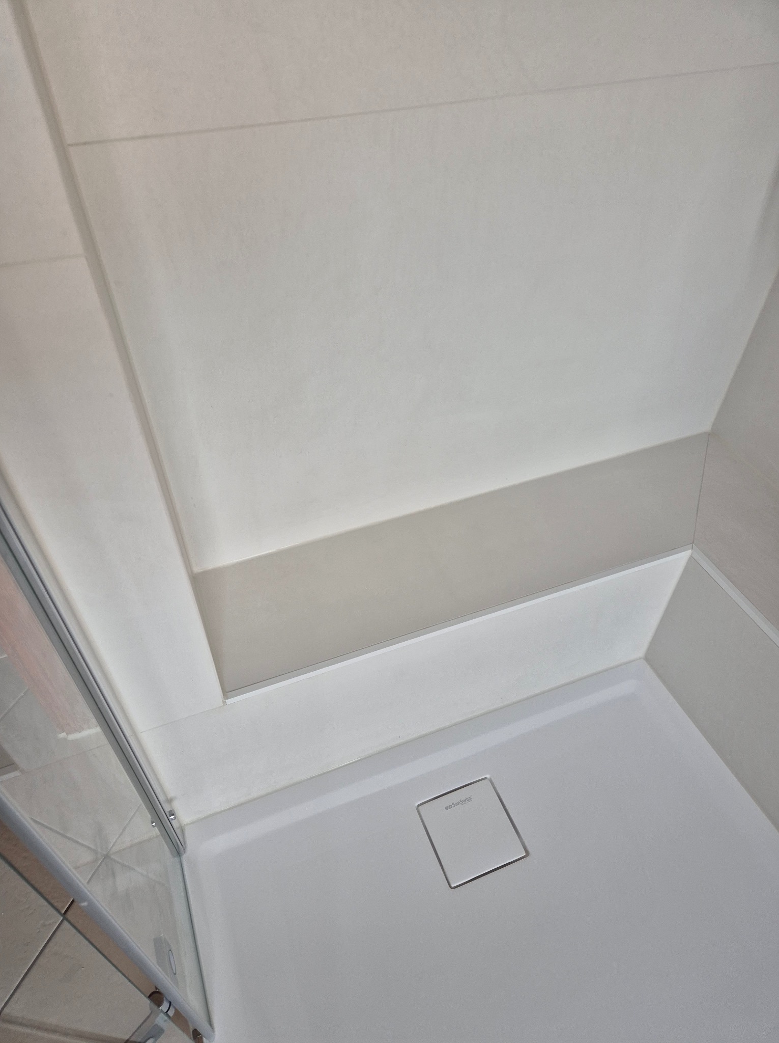 Nowoczesny brodzik z odpływem liniowym SanSwiss i kabiną prysznicową z chromowanymi profilami, widok z góry, jasne płytki na ścianach.