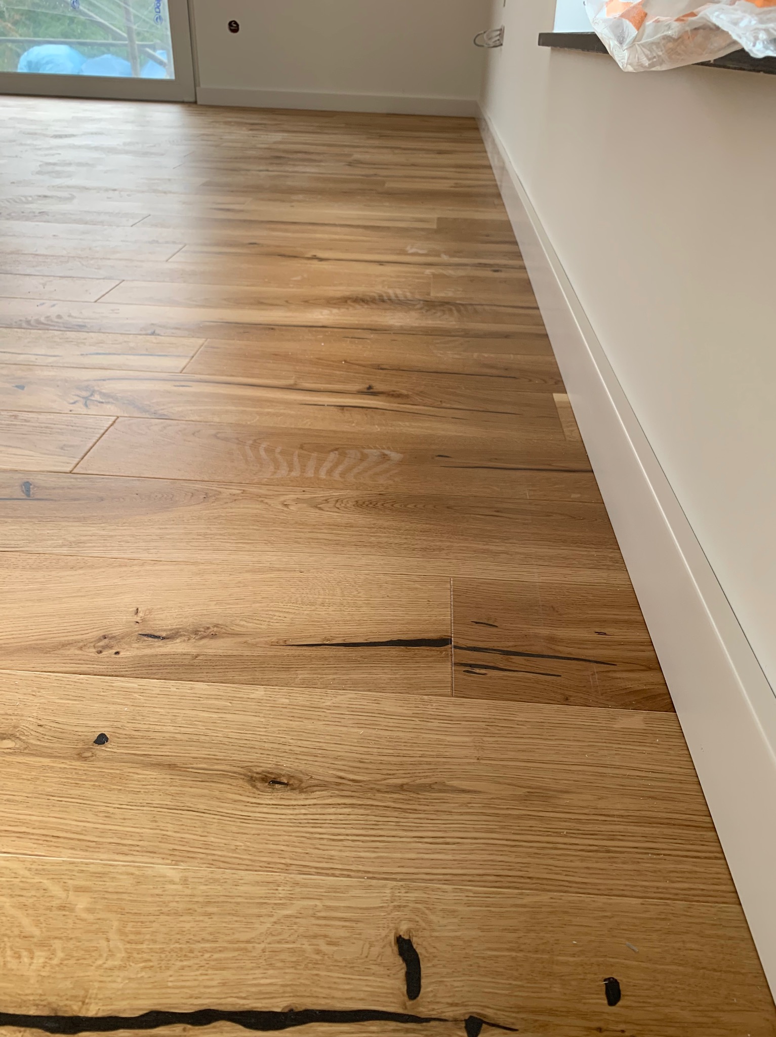 Nowo ułożona podłoga z jasnego drewna z widocznymi sękami, listwy przypodłogowe w kolorze białym, widok z niskiej perspektywy.