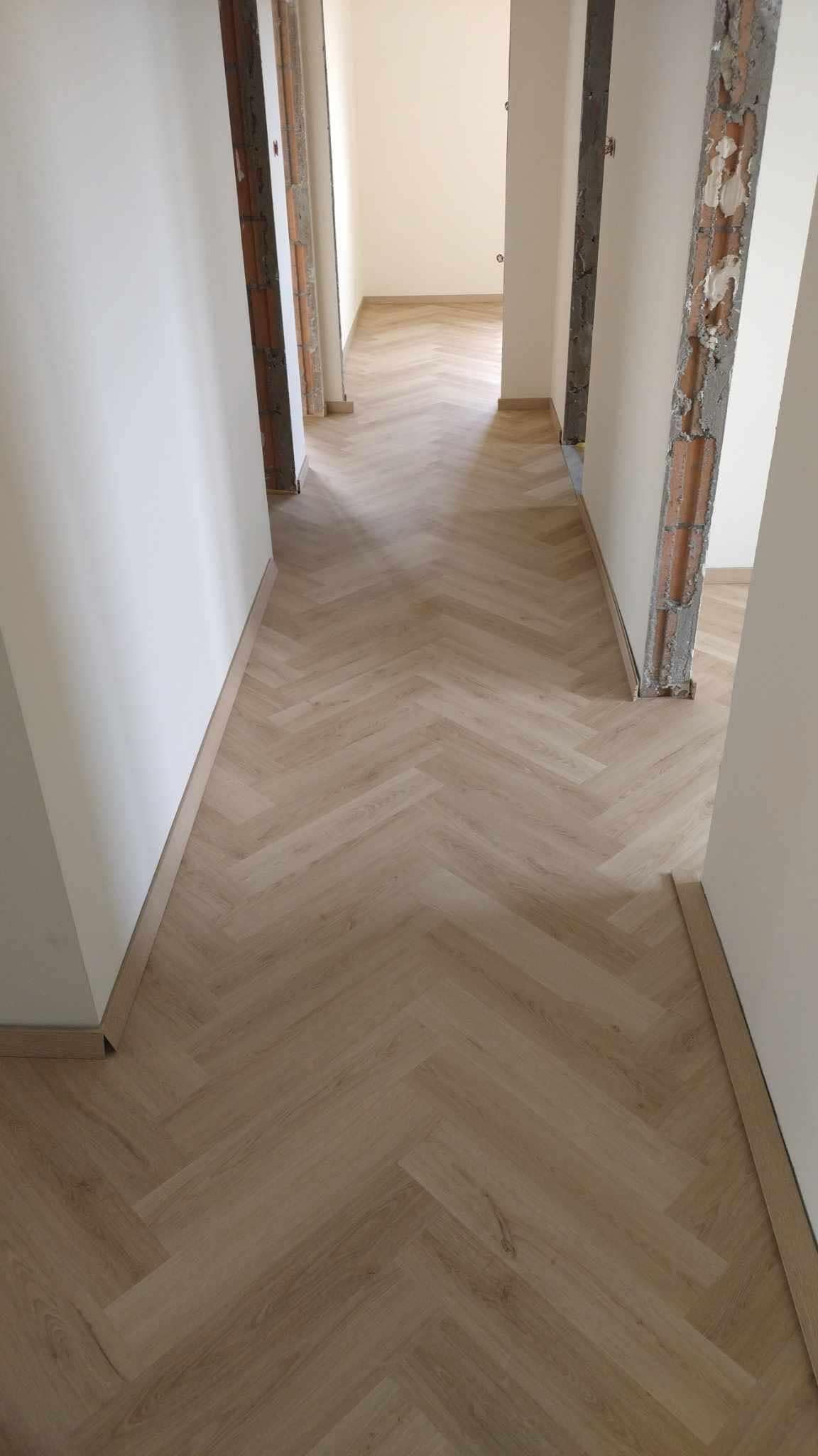 Jasne panele ułożone we wzór jodełki w korytarzu podczas remontu, widoczne surowe ściany i wykończenia.