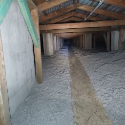 ECO-CELULOZA Piotr Kopciuch - Poddasze po ociepleniu w Rzeszowie, widoczne drewniane elementy konstrukcyjne, izolacja z wełny mineralnej oraz fragment płyty OSB tworzący ścieżkę.