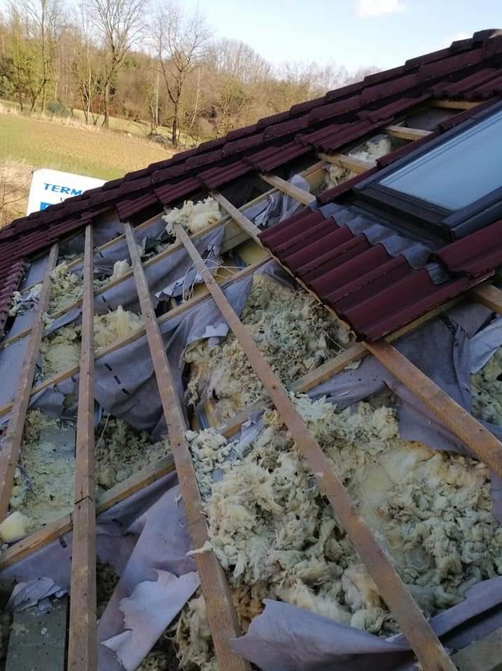 Odsłonięta konstrukcja dachu z oknem połaciowym, częściowo wypełniona wełną mineralną i zabezpieczona folią, widok z dołu na tle zieleni.