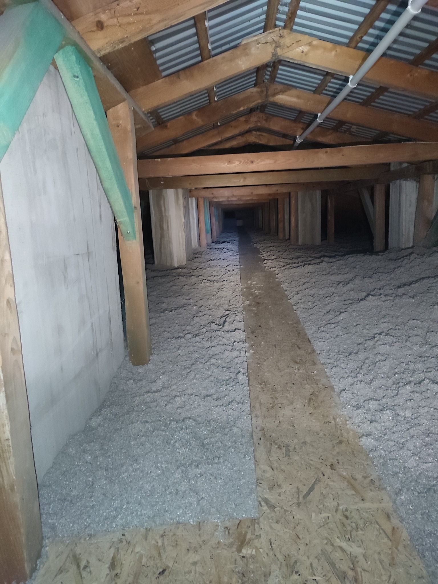 Poddasze po ociepleniu w Rzeszowie, widoczne drewniane elementy konstrukcyjne, izolacja z wełny mineralnej oraz fragment płyty OSB tworzący ścieżkę.